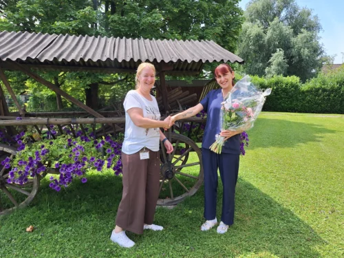 Michaela gratuliert Natasa, sie schütteln sich die Hände.Natasa hält einen Blumenstrauss in der anderen Hand.