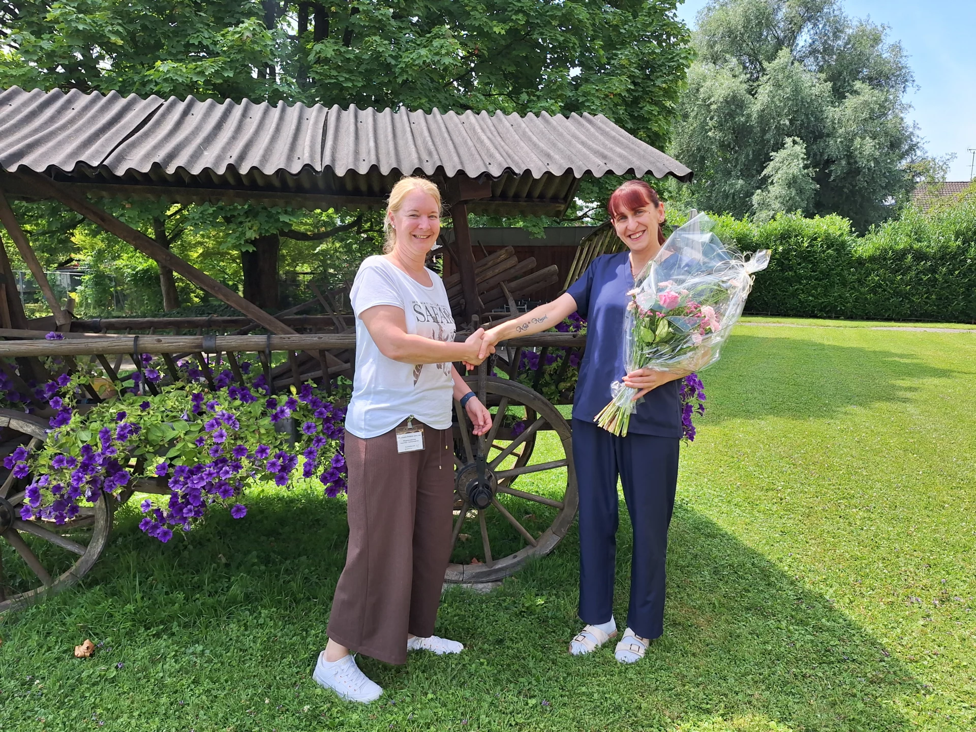 Michaela gratuliert Natasa, sie schütteln sich die Hände.Natasa hält einen Blumenstrauss in der anderen Hand.